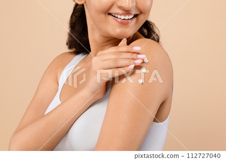 Indian woman with joyous smile delicately applying body lotion on her arm 112727040