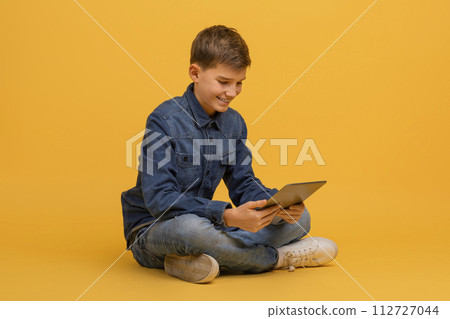 Teen boy using digital tablet while sitting cross-legged on floor in studio 112727044