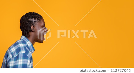 Side view of young black man shouting at free space on yellow background. Side view of young black man shouting at free space on yellow background. 112727045