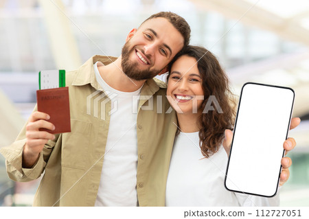 Happy Young Couple Holding Travel Tickets And Showing Smartphone With Blank Screen Happy Young Couple Holding Travel Tickets And Showing Smartphone With Blank Screen 112727051