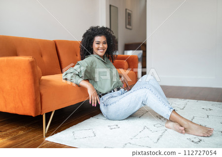 woman with bushy hair sits on floor of living room woman with bushy hair sits on floor of living room 112727054