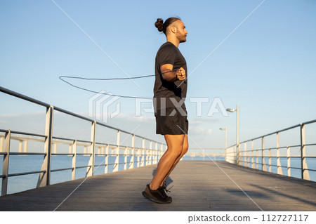 Sporty man engages in aerobics jumping with skipping rope outdoor 112727117