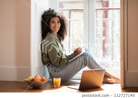 Cheerful brazilian woman sitting with her notebook and laptop indoor 112727140