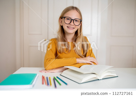 Nerdy teenage girl wearing glasses sitting at her desk with open book Nerdy teenage girl wearing glasses sitting at her desk with open book 112727161