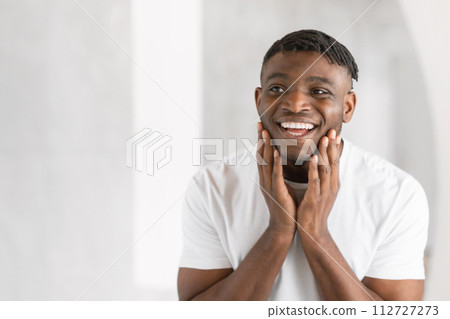 Young African American man smiles happily touching face in bathroom 112727273
