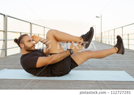 Motivated man in activewear works on abs doing bicycle crunches 112727291