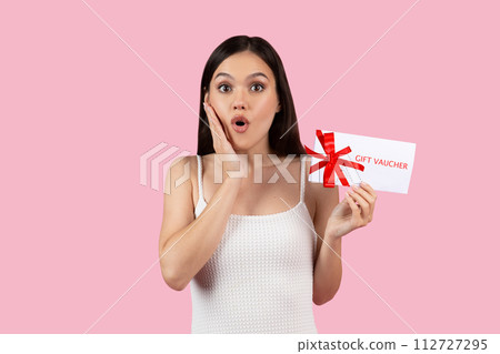Surprised young woman holding gift voucher with red bow 112727295