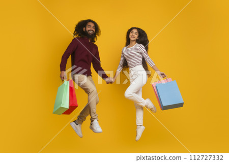 Emotional young indian couple jumping with shopping bags 112727332