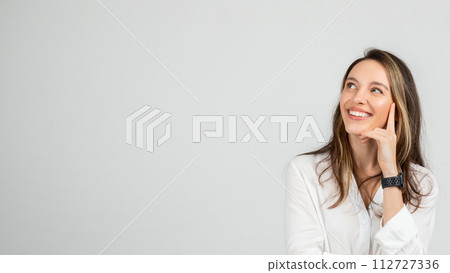 Dreamy young woman with a joyful smile looking upwards, resting her face on her hand 112727336