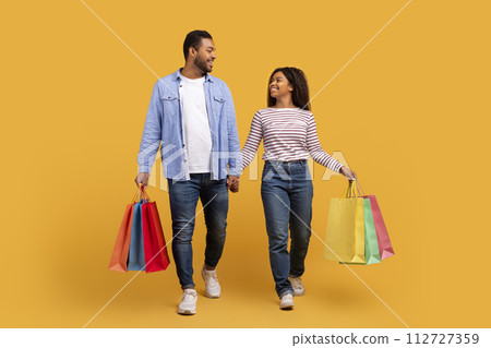 Smiling black couple carrying bright shopping bags, walking and holding hands 112727359