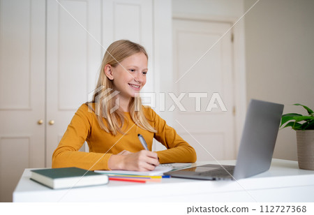 Online Education Concept. Smiling young teenage girl using laptop and taking notes Online Education Concept. Smiling young teenage girl using laptop and taking notes 112727368