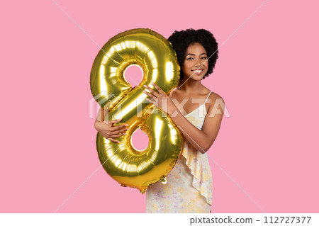 Radiant young woman with curly hair holding a golden number 8 balloon, celebrating a special occasion Radiant young woman with curly hair holding a golden number 8 balloon, celebrating a special occasion 112727377