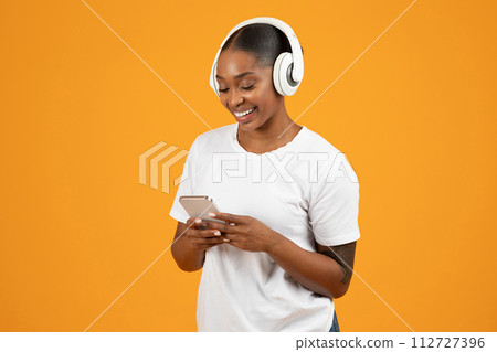 African American woman with mobile phone in headphones, orange studio African American woman with mobile phone in headphones, orange studio 112727396