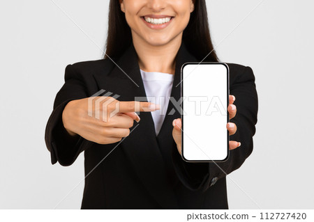 Happy woman in business attire presenting smartphone screen Happy woman in business attire presenting smartphone screen 112727420