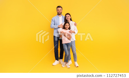Father, mother and daughter smiling standing together against yellow backdrop 112727453