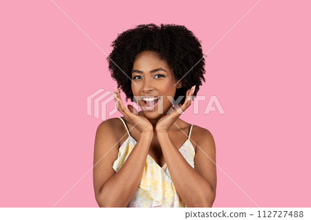 An exuberant young African American woman with curly afro hair joyfully holds her face An exuberant young African American woman with curly afro hair joyfully holds her face 112727488