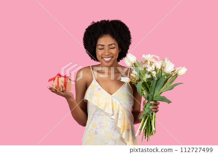 Spirited African American woman with curly hair blissfully holding a bouquet of white tulips Spirited African American woman with curly hair blissfully holding a bouquet of white tulips 112727499