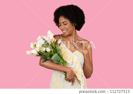 Content African American woman with a natural hairstyle admiring a beautiful bouquet of mixed flowers 112727515
