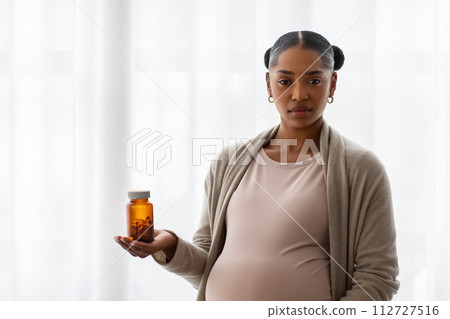 Serious pregnant black woman showing jar with medicine 112727516