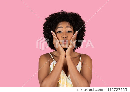 Playful African American woman with curly hair making a funny face with puffed cheeks Playful African American woman with curly hair making a funny face with puffed cheeks 112727535