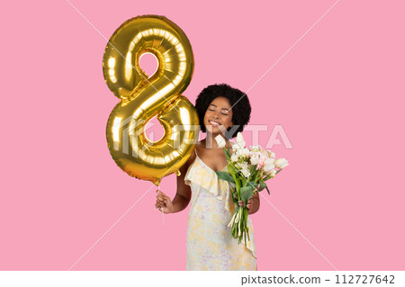 Happy African American woman with a natural hairstyle celebrating with a golden number 8 balloon 112727642