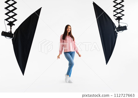Joyful lady model in casual attire mid-twirl in well-equipped photo studio with white backdrop Joyful lady model in casual attire mid-twirl in well-equipped photo studio with white backdrop 112727663
