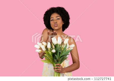 Charming African American woman with curly hair playfully blowing a kiss 112727741