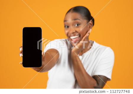 Excited black woman extends arm showing smartphone empty screen, studio Excited black woman extends arm showing smartphone empty screen, studio 112727748