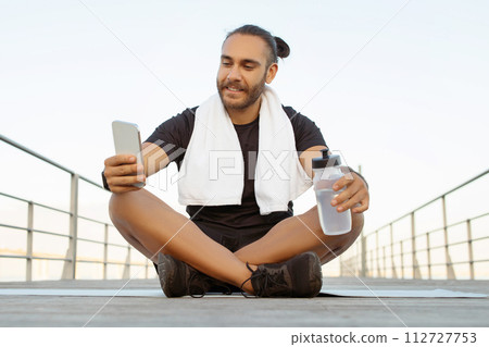athlete man enjoys break sitting with phone after outdoor workout athlete man enjoys break sitting with phone after outdoor workout 112727753