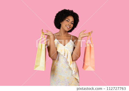 Cheerful young woman with curly hair blissfully holding colorful shopping bags 112727763