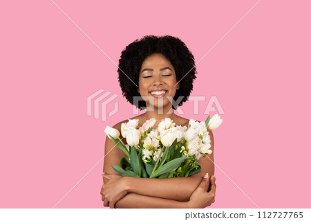 Content young African American woman with eyes closed, a serene smile, embracing a lush bouquet Content young African American woman with eyes closed, a serene smile, embracing a lush bouquet 112727765