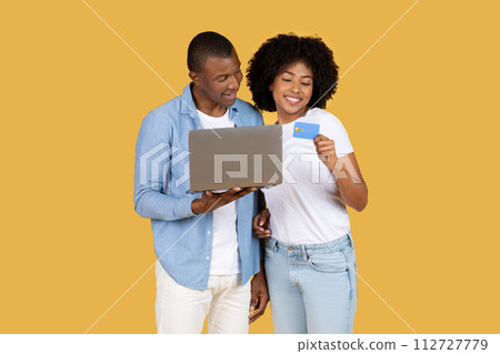 A couple engages with online shopping, the woman holding a credit card and the man holding a laptop 112727779