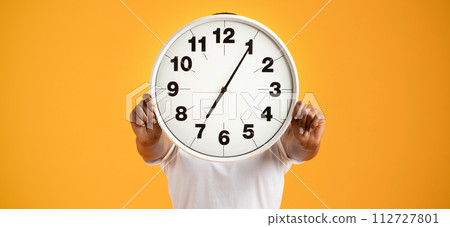 black lady poses with clock covering head against orange background 112727801