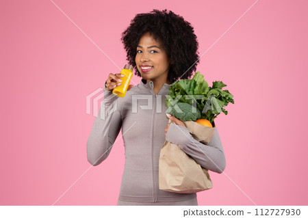 Cheerful black woman sipping juice, holding grocery bag Cheerful black woman sipping juice, holding grocery bag 112727930