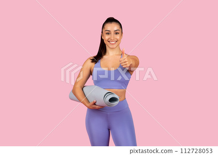 Positive young woman with yoga mat giving thumbs up Positive young woman with yoga mat giving thumbs up 112728053