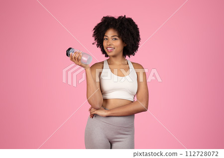 Smiling black woman with water bottle, sportswear, pink background 112728072