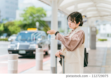 一位年輕的女商人在車站、航站樓或公車站檢查手錶上的時間（遲到、延誤、不耐煩、惱怒） 112729075