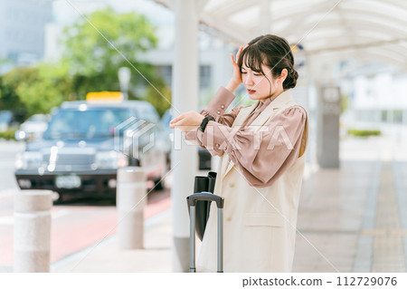 A young business woman checking the time on her wristwatch at a station, terminal, or bus stop (late, delayed, impatient, irritated) 112729076