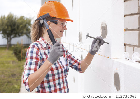 Insulation of the house with polyfoam. The worker is checking with the construction level the accuracy of the installation of polystyrene board on the facade. Insulation of the house with polyfoam. The worker is checking with the construction level the accuracy of the installation of polystyrene board on the facade. 112730065
