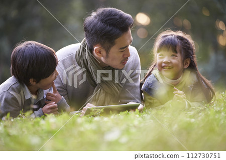 asian father and two children relaxing outdoors in city park asian father and two children relaxing outdoors in city park 112730751