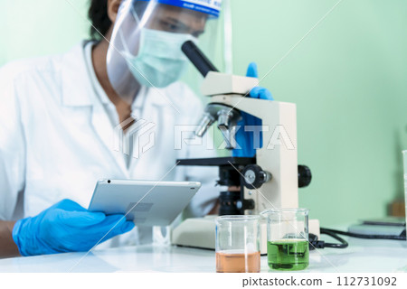 Indian Scientist man look into Microscope research in science laboratory. Asian biochemistry scientist using microscope in laboratory chemistry labs. Covid-19 medical research scientific experiment 112731092