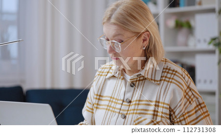 A confident senior woman is working on her laptop in her home office, embracing the freelancer's lifestyle A confident senior woman is working on her laptop in her home office, embracing the freelancer's lifestyle 112731308