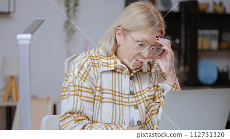 A woman in her 50s is tired from computer work in her home office, feeling exhausted 112731320