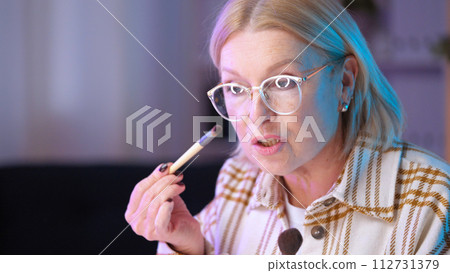 A woman in her 50s is recording a makeup tutorial for her beauty channel while holding brushes A woman in her 50s is recording a makeup tutorial for her beauty channel while holding brushes 112731379