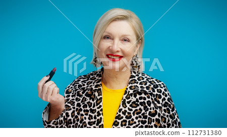 A beautiful senior woman is applying red lipstick and smiling, showcasing anti-aging cosmetics A beautiful senior woman is applying red lipstick and smiling, showcasing anti-aging cosmetics 112731380