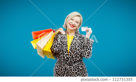 A happy senior woman with shopping bags is showing her credit card for online payment 112731385