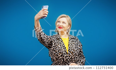 A senior female influencer is taking a selfie on her phone as part of a social media challenge 112731400