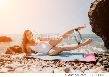 Woman sea fitness. Happy woman with long hair, fitness instructor in white bikini doing stretching and pilates on yoga mat near the sea. Female fitness yoga routine concept. Healthy lifestyle. 112733360