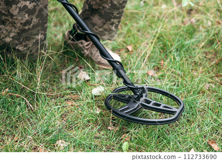 Soldier using a metal detector in fields. Ukrainian Explosive Ordnance Disposal Officer detecting metal by metal detector device Soldier using a metal detector in fields. Ukrainian Explosive Ordnance Disposal Officer detecting metal by metal detector device 112733690