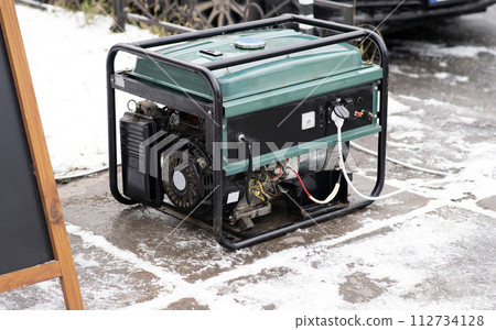 Portable electric generator running in the cold winter.Energy genocide. Power outage as a result of missile strikes by Russia on energy facilities of Ukraine. Small business use gasoline generators. 112734128